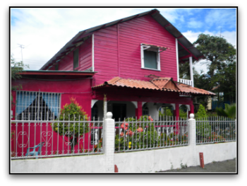 Hot pink wooden house with flowers and white cement fence