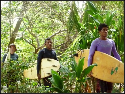 3 guys walking with surfboards through the jungle