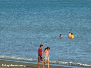 couple walking down beach, 3 people standing in the ocean