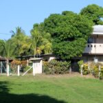 Photo of flat grassy area , fence posts, house, and trees