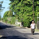 Photo of a man with hat walking down a paved road