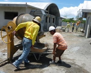 2 men at a cement mixer, more behind building 2 vaulted buildings
