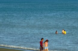 Photo of a couple walking down the beach & people in the ocean