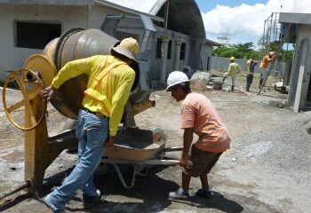 2 men at a cement mixer, more behind building 2 vaulted buildings