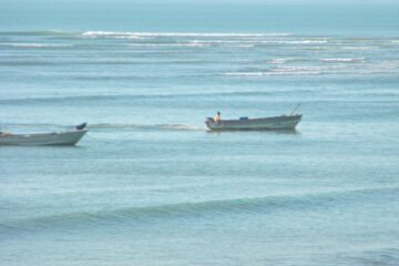 calm ocean with 2 fishing boats going by close to shore