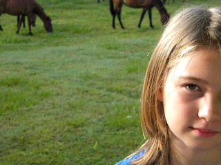 close up, partial view, of young girl, green grass with horses grazing in background