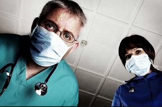 doctor & nurse with surgical masks on peering down at patient