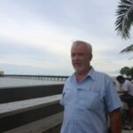 Older man in blue shirt standing by beach railing