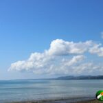 Blue sky with puffy white clouds , ocean, and pennisula in distance