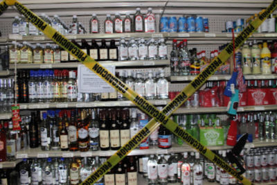 Photo of liquor shelves with big x of yellow tape over it. 
