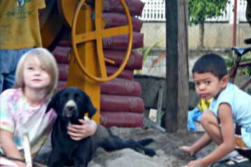 2 children and 1 dog playing in sand by cement mixer