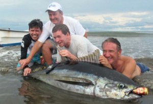 4 men hanging out on the beach with a fish they caught.