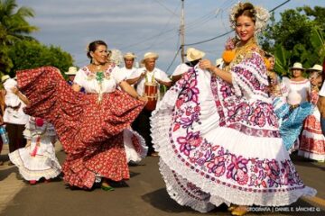 2 women dancing in traditional Panamanian clothes followed by men drumming