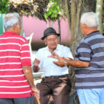 1 man wearing a fedora and 2 men facing him - all chatting