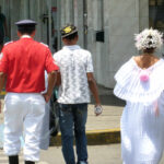 3 people walking away: military man, young man with baseball hate, and young woman in traditional Panamanian costume