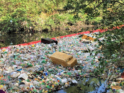 garbage in a river corraled between the shore and a floating plastic barrier